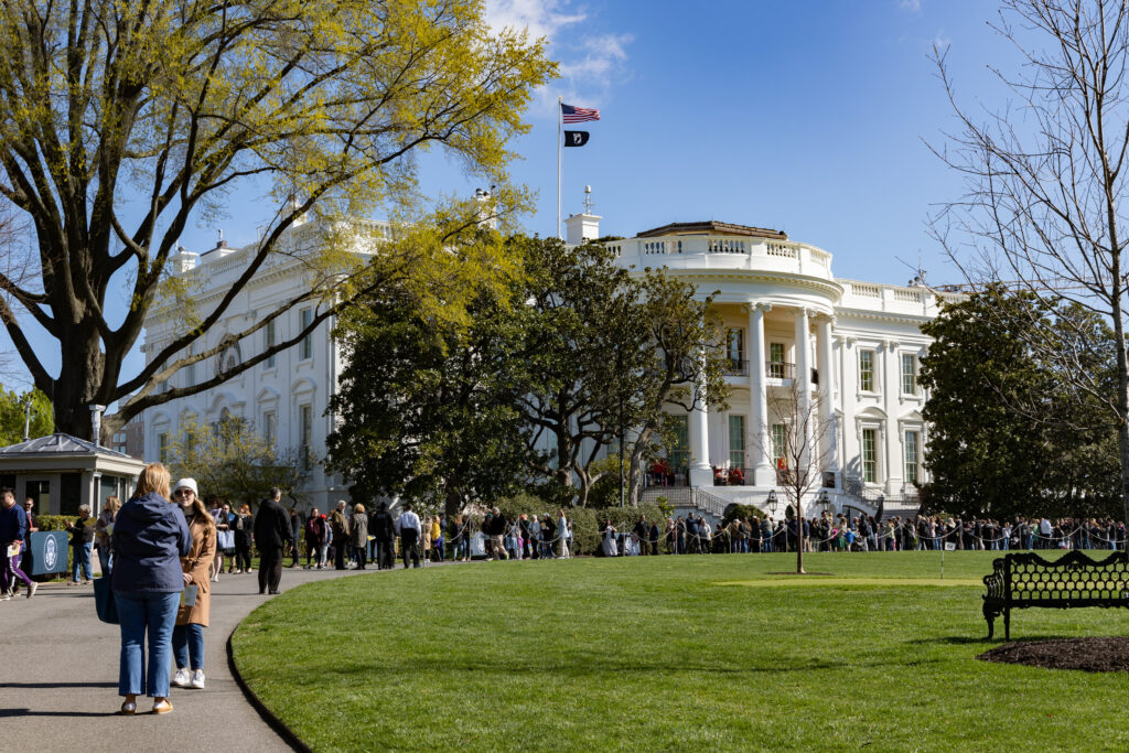 A large group of visitors walk on the white house grounds.